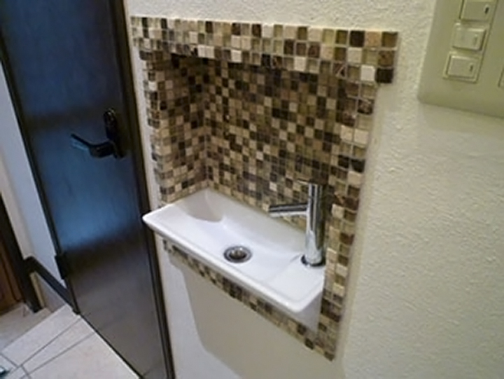 トイレの手洗いを、玄関ホールの壁のニッチ部分に設けました。<br />
キッチンと同じモザイクタイルを使用しました。
